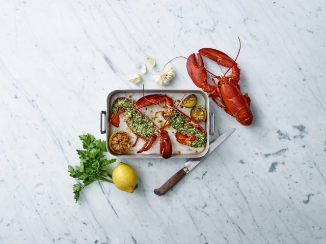 a lobsters on a pan next to a knife and lemon
