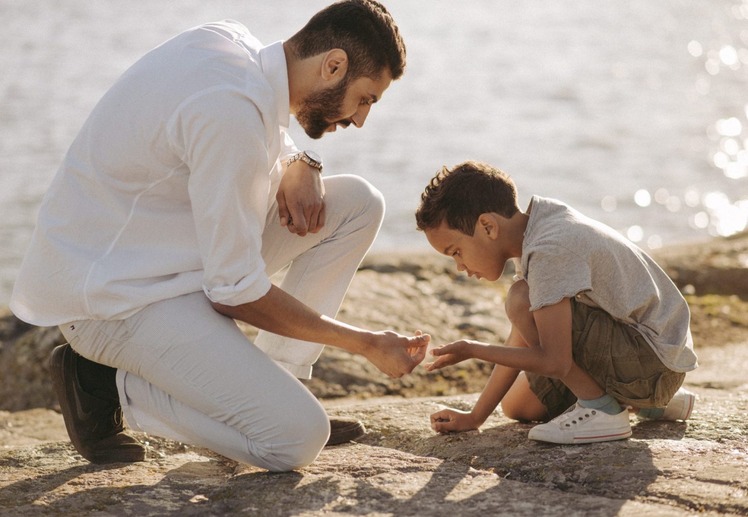 a man and boy kneeling on a rock by water