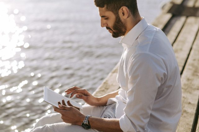 a man sitting on a ledge looking at a tablet