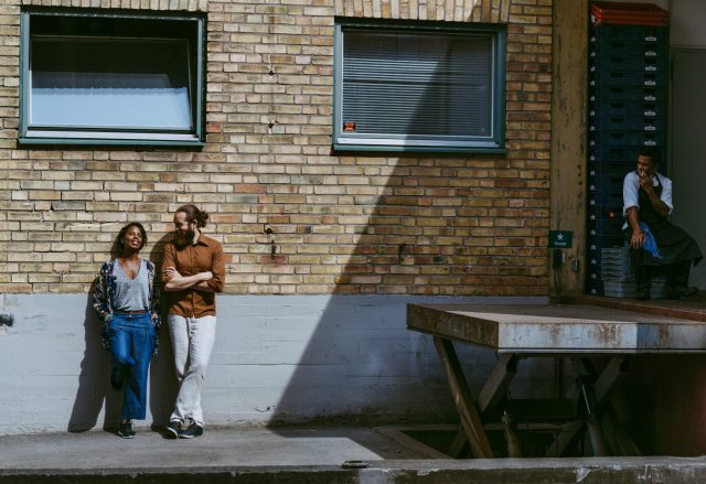 a man and woman leaning against a brick wall