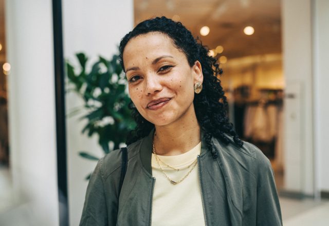 a woman with curly hair wearing a green jacket and gold earrings