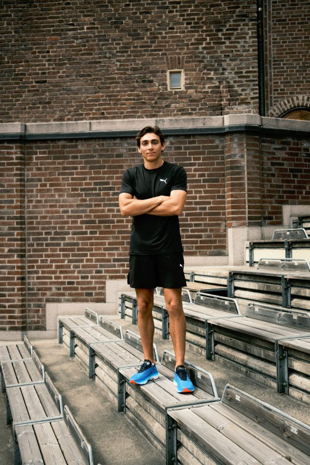 Young man in black Puma athletic wear standing on bleachers.