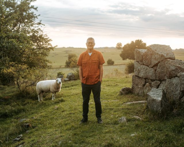 a man standing in a grassy field with a sheep
