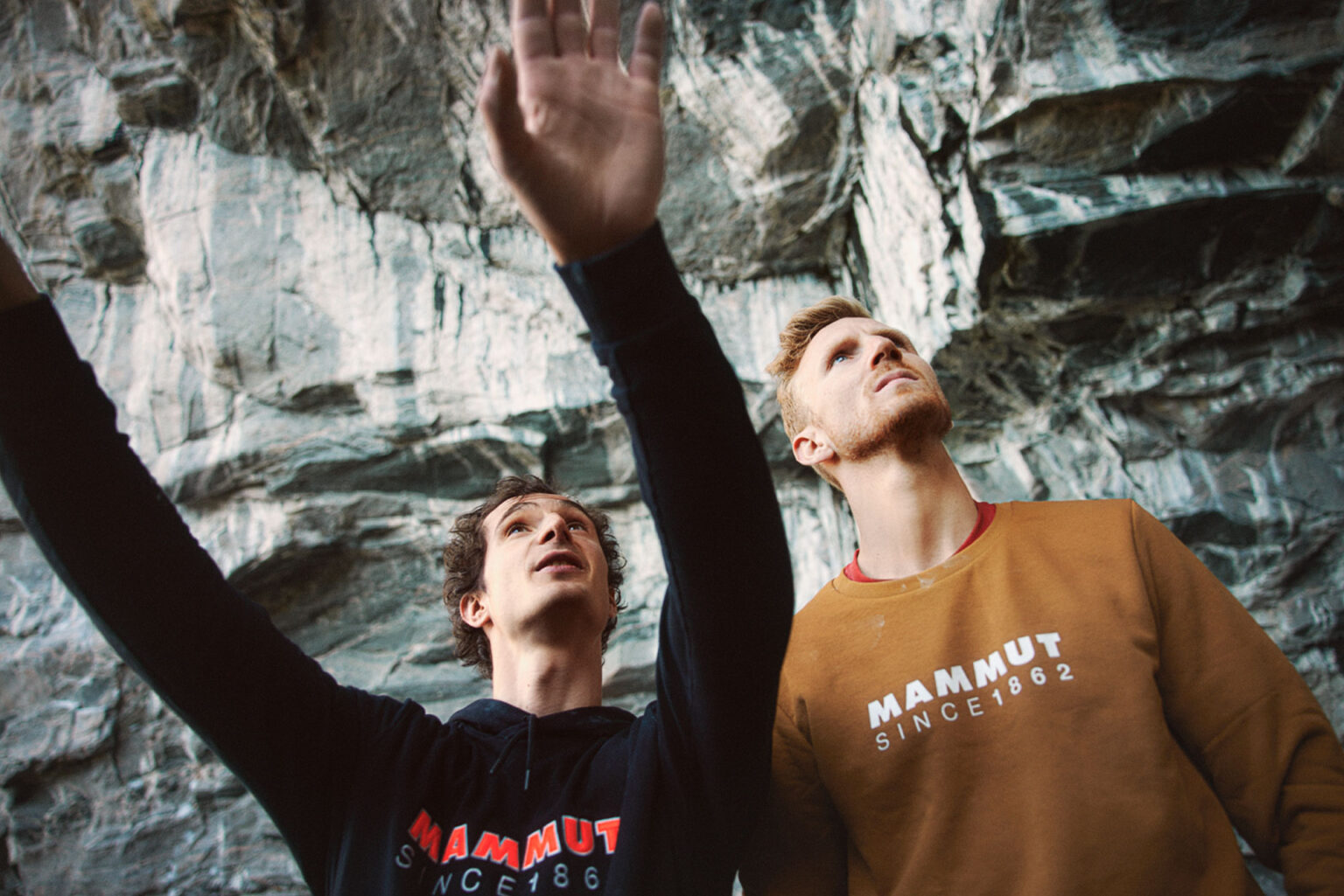 two men standing in front of a rock wall