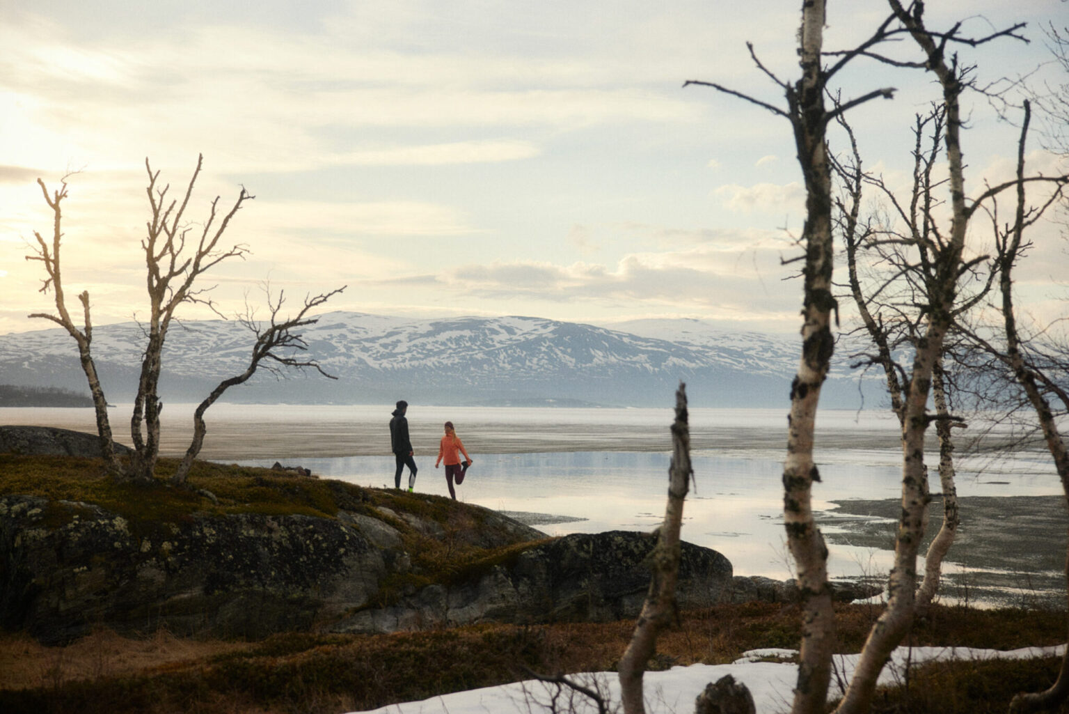 a couple of people walking on a rocky hill by a body of water