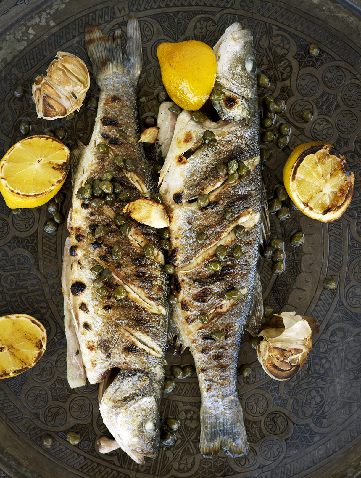 a fish with capers and lemons on a plate