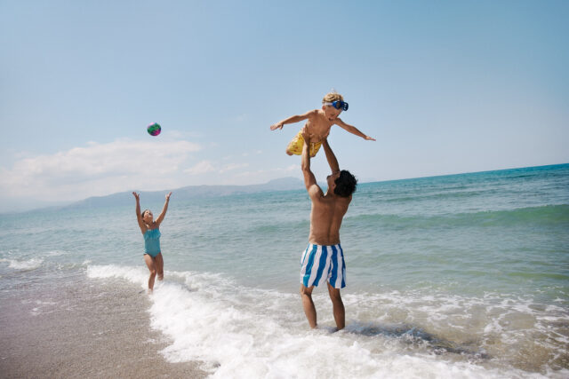 a man lifting a child up in the air on a beach