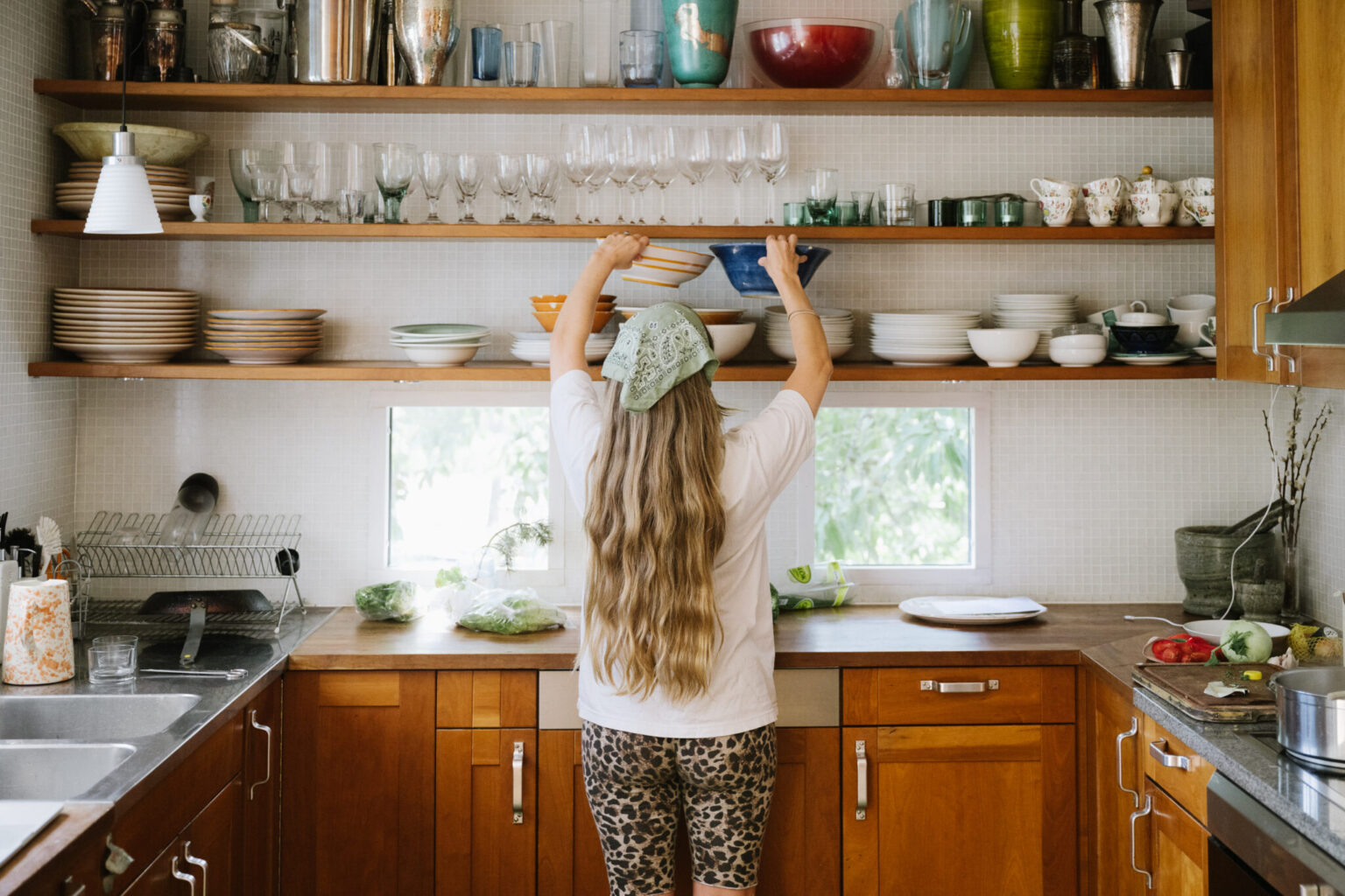 a woman in a kitchen with a shelf full of dishes