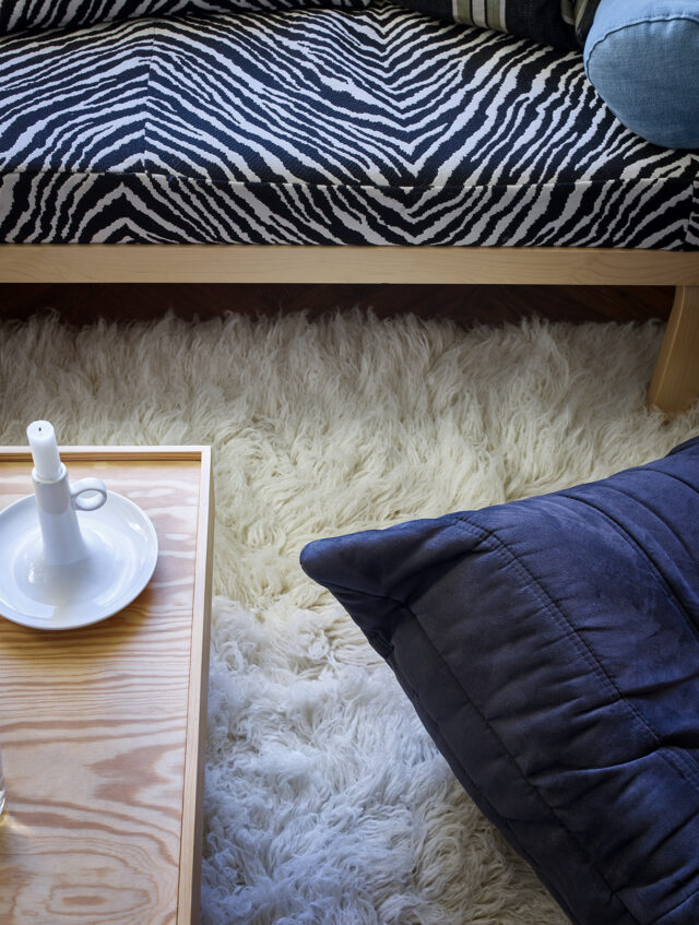 Zebra print sofa above a fluffy white rug and a dark blue cushion.