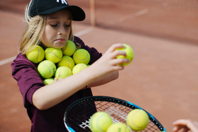 a girl holding a tennis racket and a pile of balls