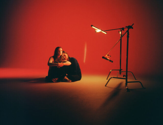 a couple sitting on the floor in front of a red wall