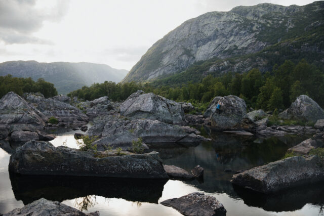 a person standing on rocks in a river surrounded by mountains