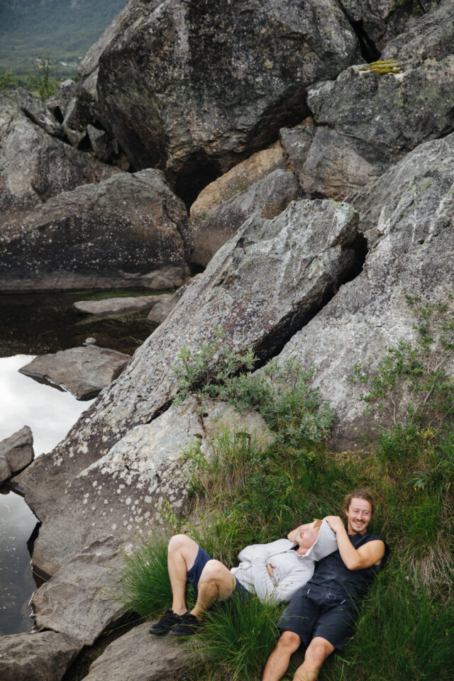 a man and woman lying on grass next to rocks