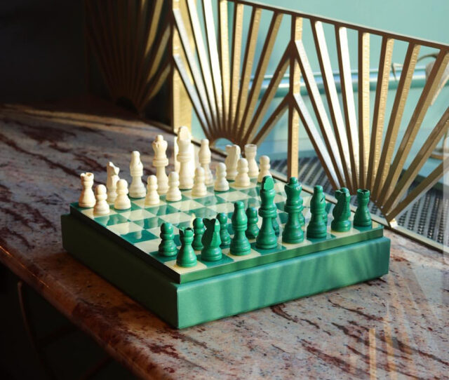 a chess board with green and white pieces on a marble surface