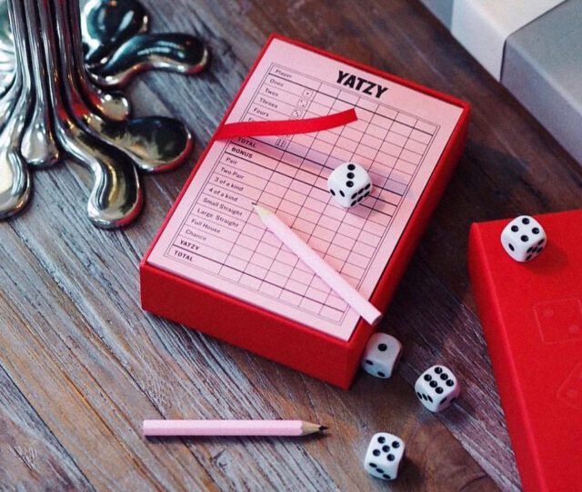 a red box with dice and pencil on a wood surface