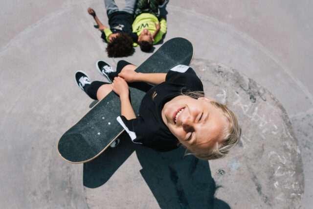 a boy sitting on a skateboard with another boy behind him