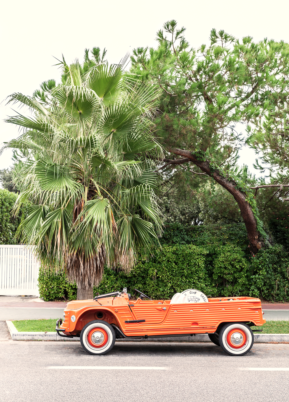 an orange car parked on the side of a road next to a palm tree
