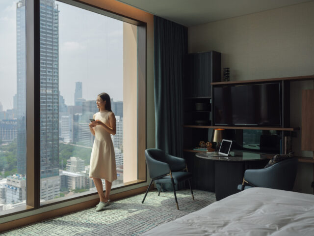 a woman standing in a hotel room looking out a window