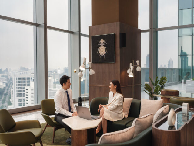 a man and woman sitting on a couch in a room with large windows