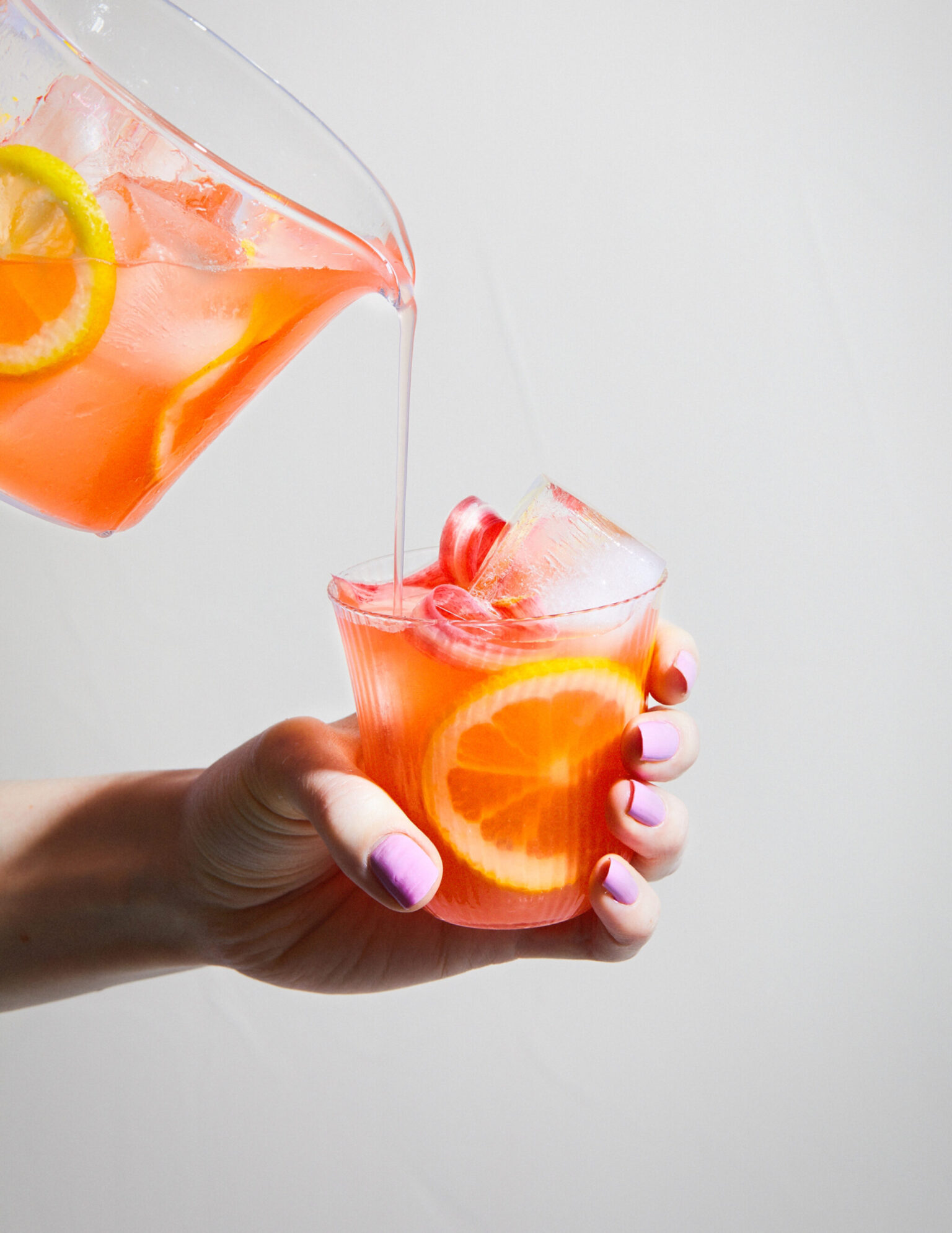 a hand holding a glass with a drink and a pitcher