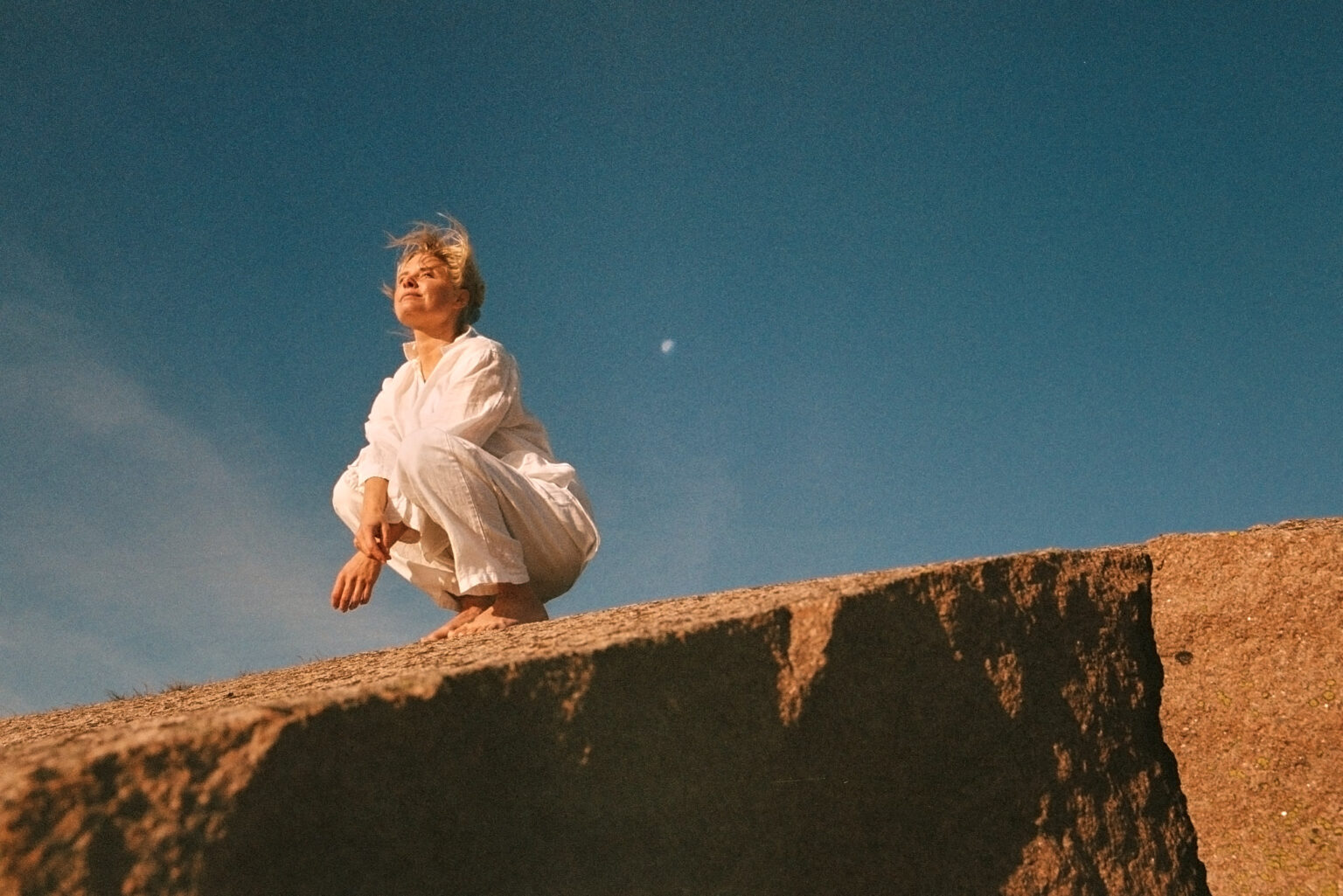 a woman in white clothes squatting on a rock