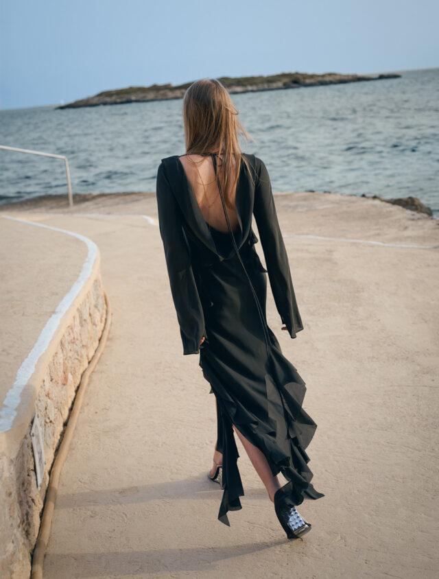 a woman in a black dress walking on a dock