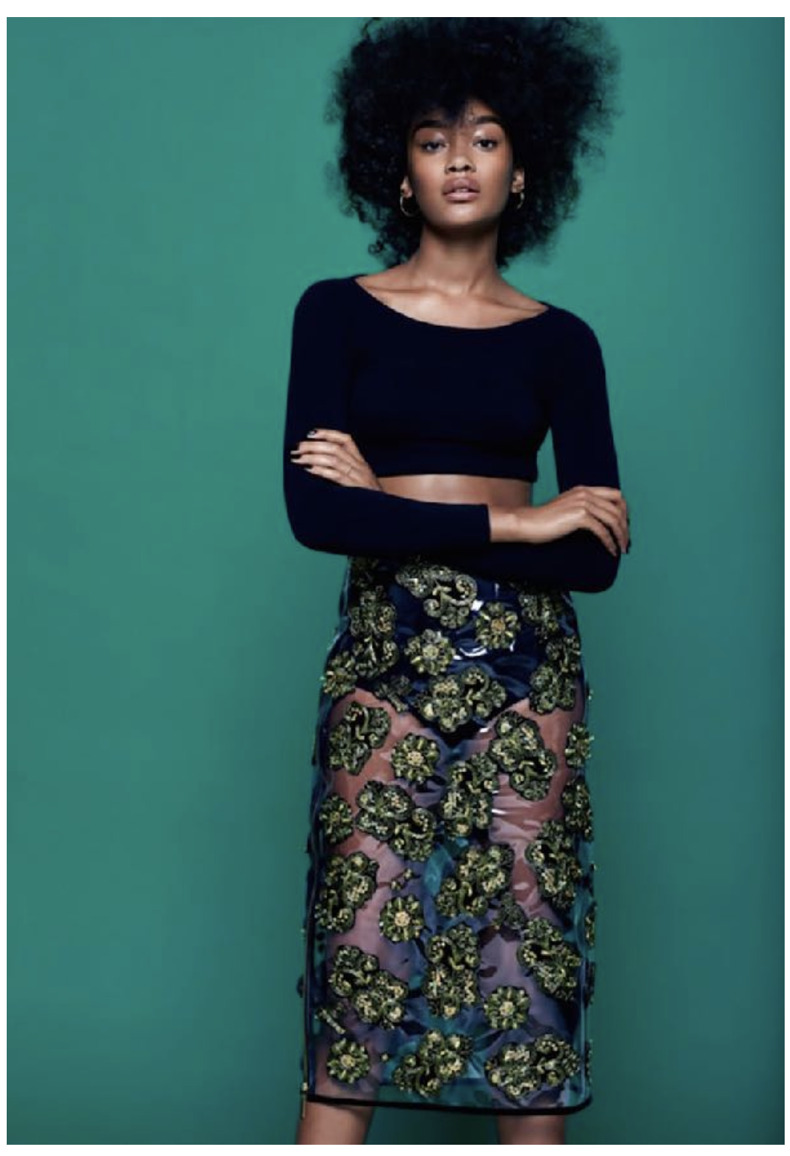 a woman with curly hair wearing a blue top and a floral skirt