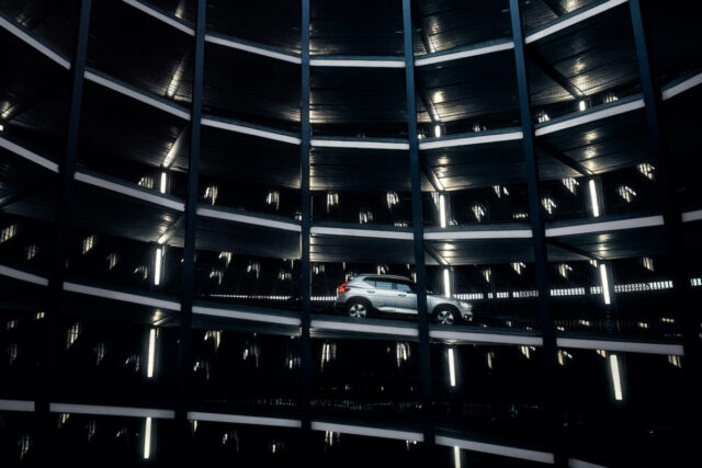 Silver car parked on a level of a dark, multi-story parking garage with bright lights.