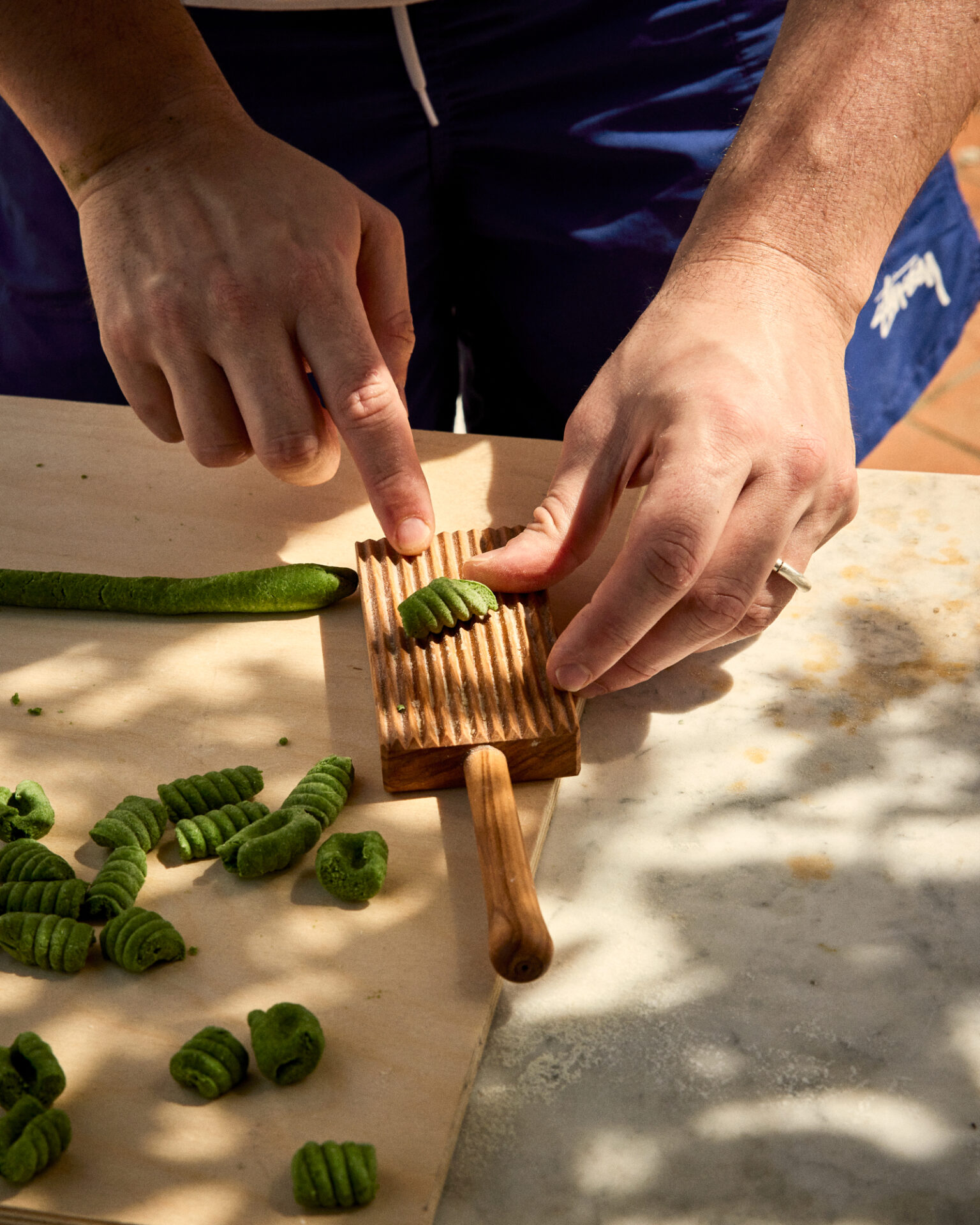 a person using a wood cutting board to cut green pasta