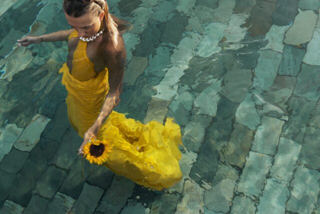a woman in a yellow dress holding a sunflower in water