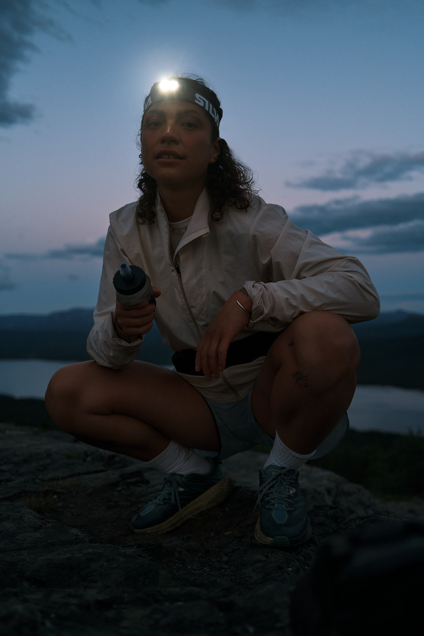 a woman squatting on a rock with a water bottle