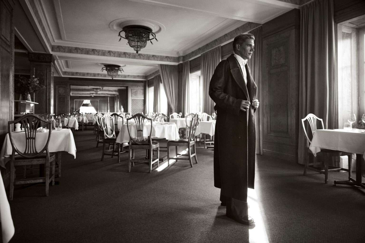 a man in a long coat in a room with tables and chairs