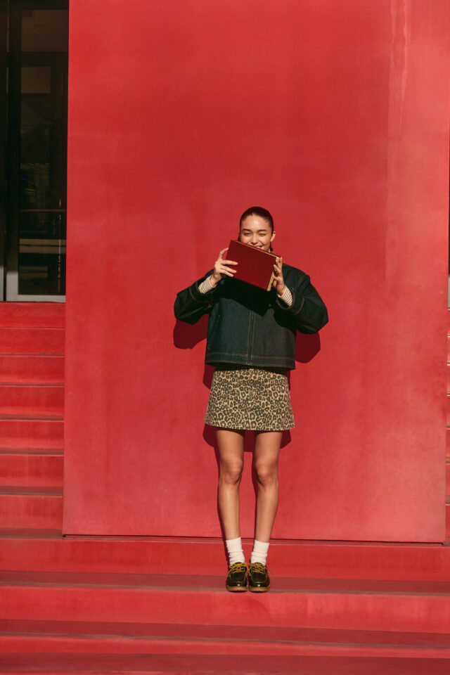 a woman holding a book in front of a red wall