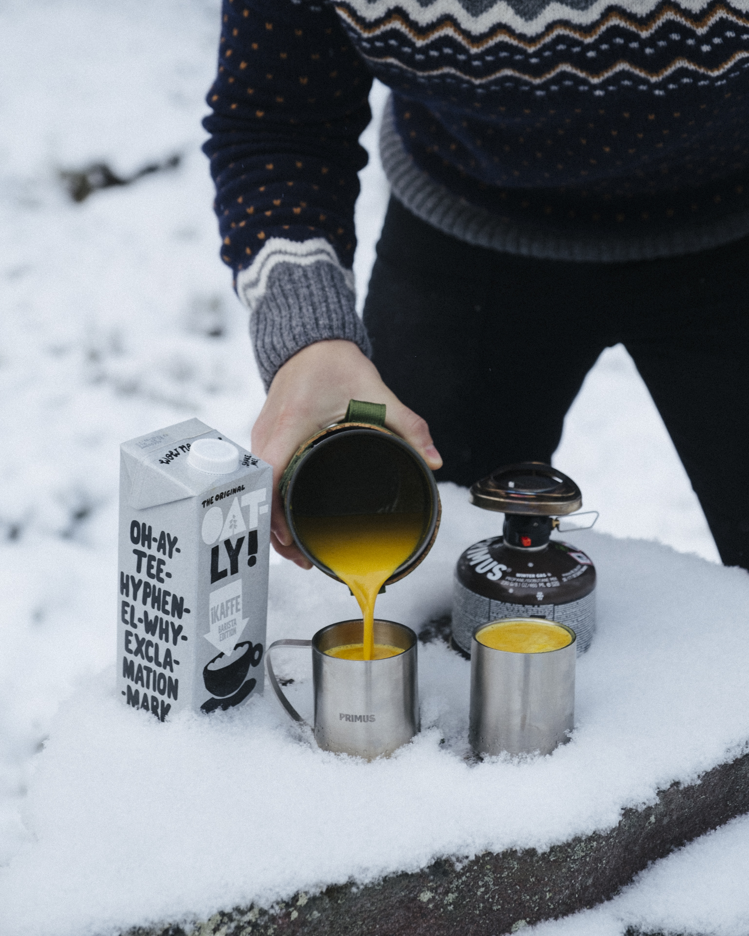 a person pouring yellow liquid into cups on snow