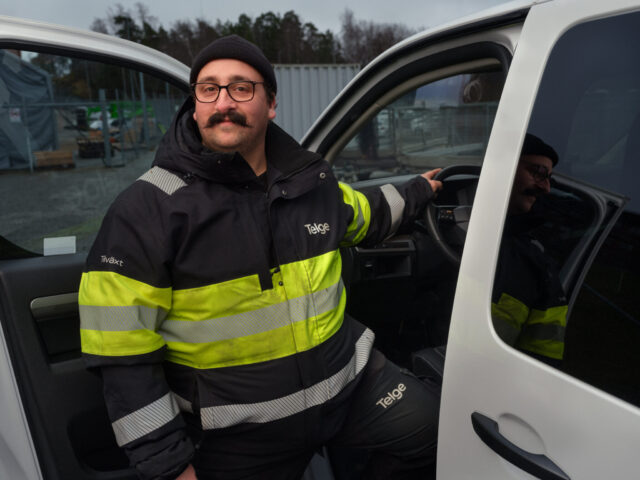 a man in a yellow and black jacket and hat with a mustache leaning on a steering wheel of a car