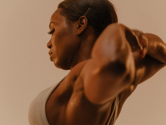 Woman with muscular arms and back, profile view, light background.