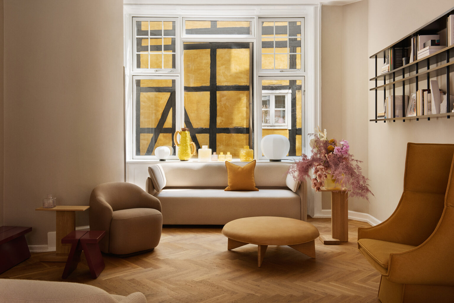 A modern living room with a beige sofa, accent chairs, and a round ottoman on a herringbone floor.
