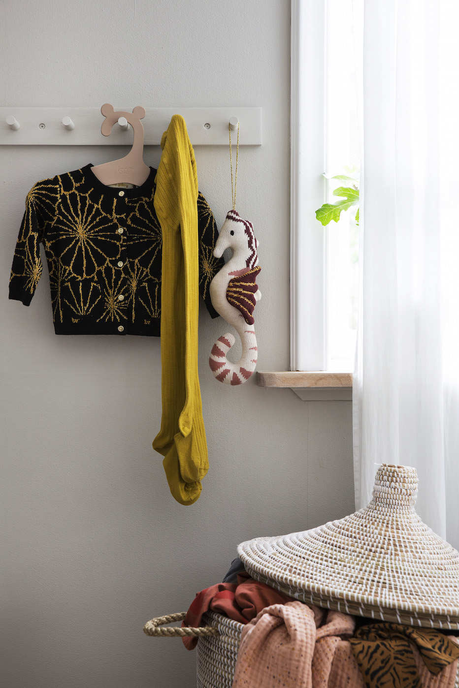 A black and gold cardigan, yellow tights, and a seahorse toy hang on a wall rack.