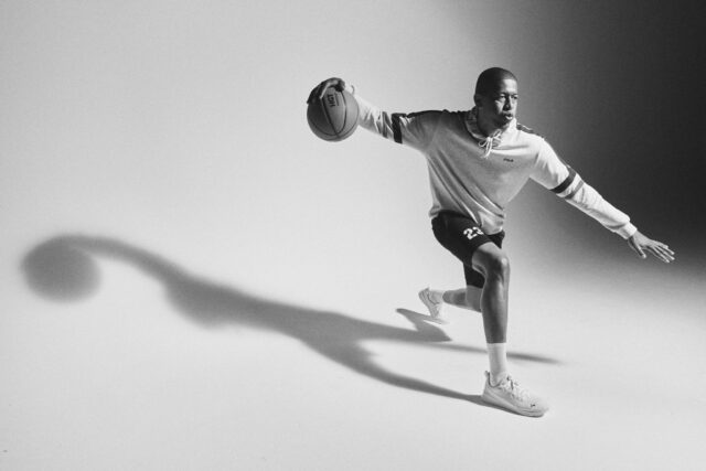 Black and white photo of a basketball player dribbling, with a long shadow.