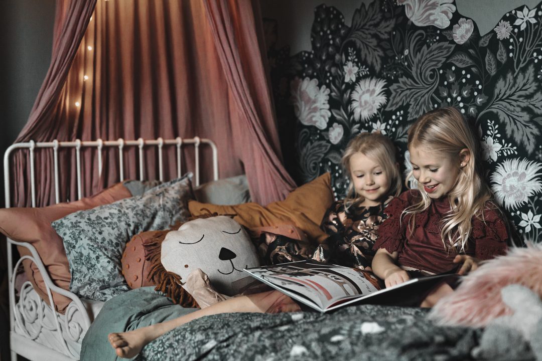 Two girls reading a book in a cozy bedroom with a canopy bed.