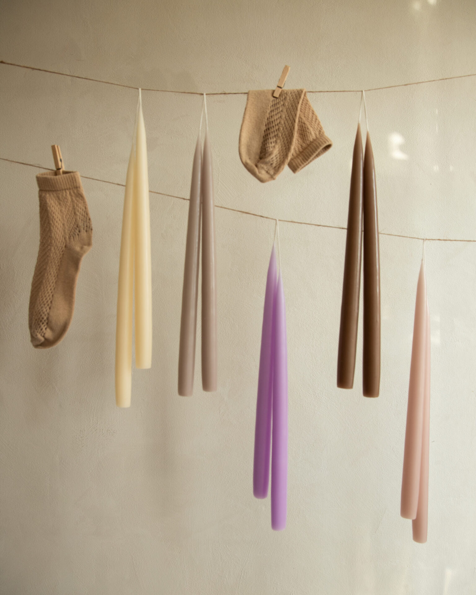 Taper candles in various colors and two knitted socks hang from a clothesline.