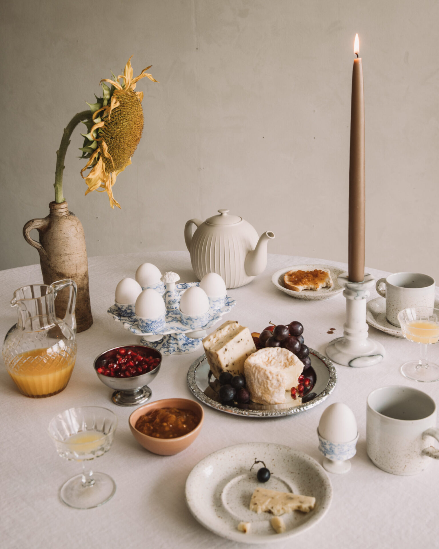 Breakfast table with eggs, cheese, fruit, toast, juice, and a lit candle.