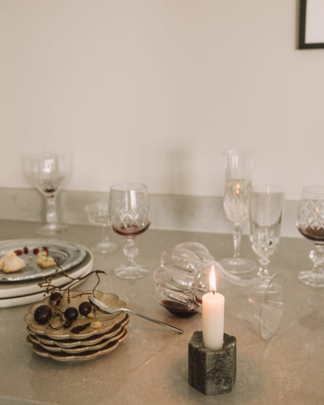 A lit candle on a table with wine glasses, grapes, and plates.