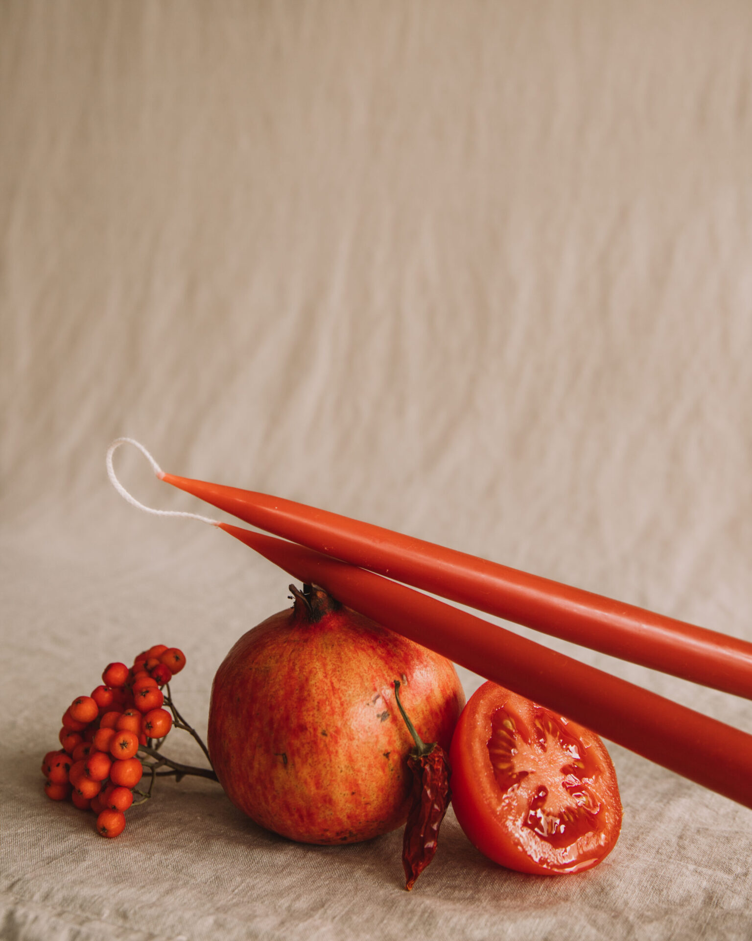 Two red candles over pomegranate, tomato, chili, and berries on linen.