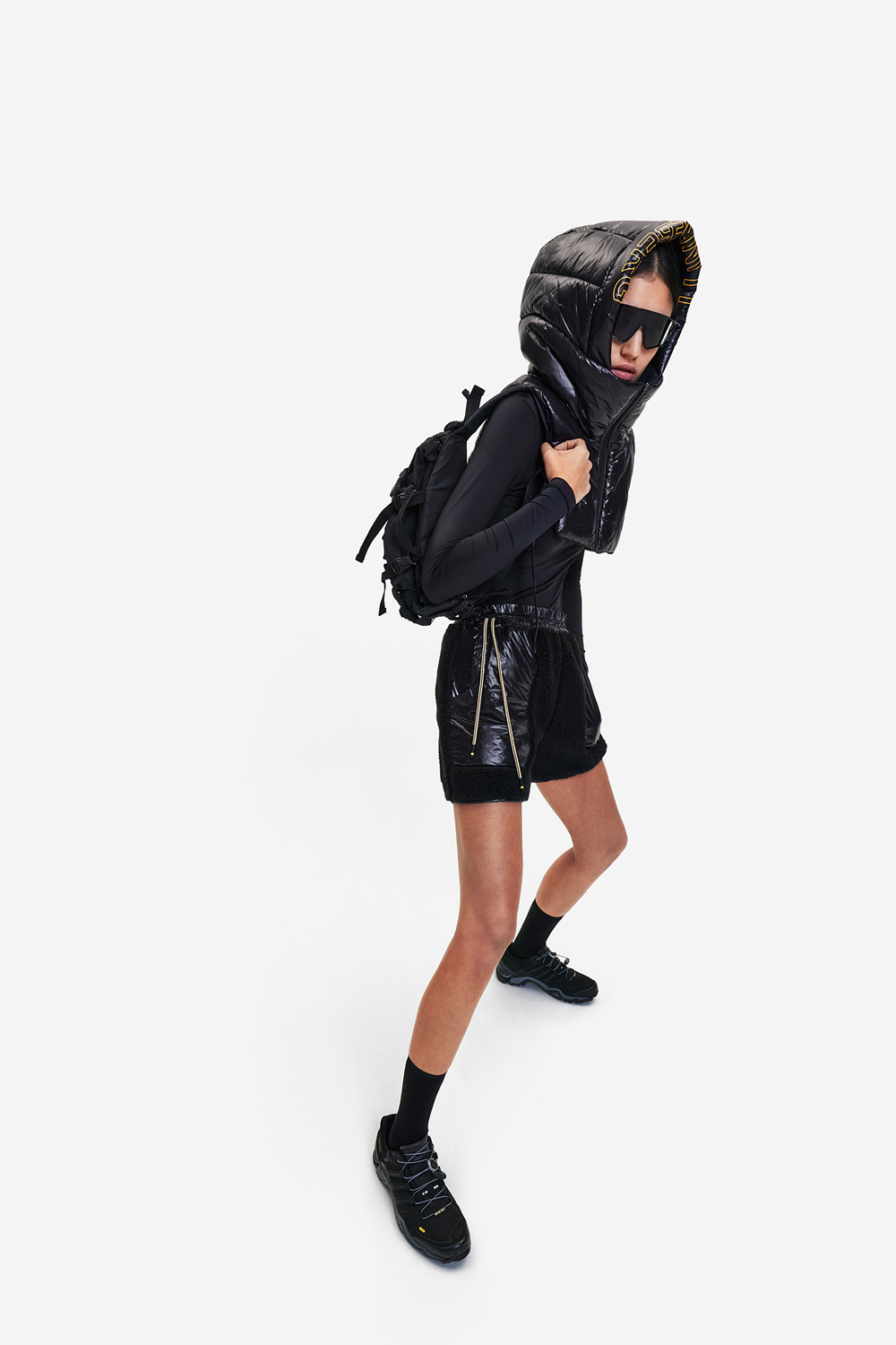Woman in black puffer vest, shorts, and sneakers with backpack.