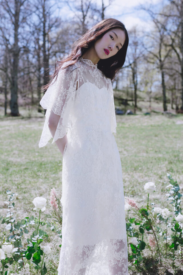 Woman in white lace dress in a garden with white roses.