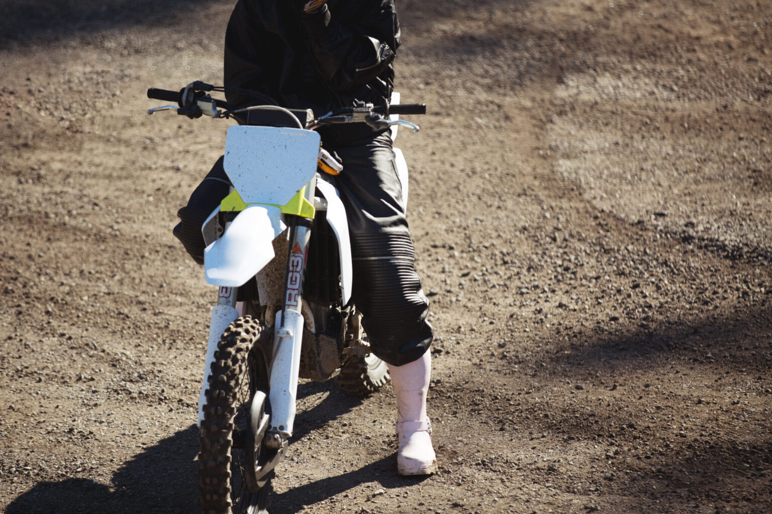 Motocross rider on a dirt track, wearing black gear and pink boots.