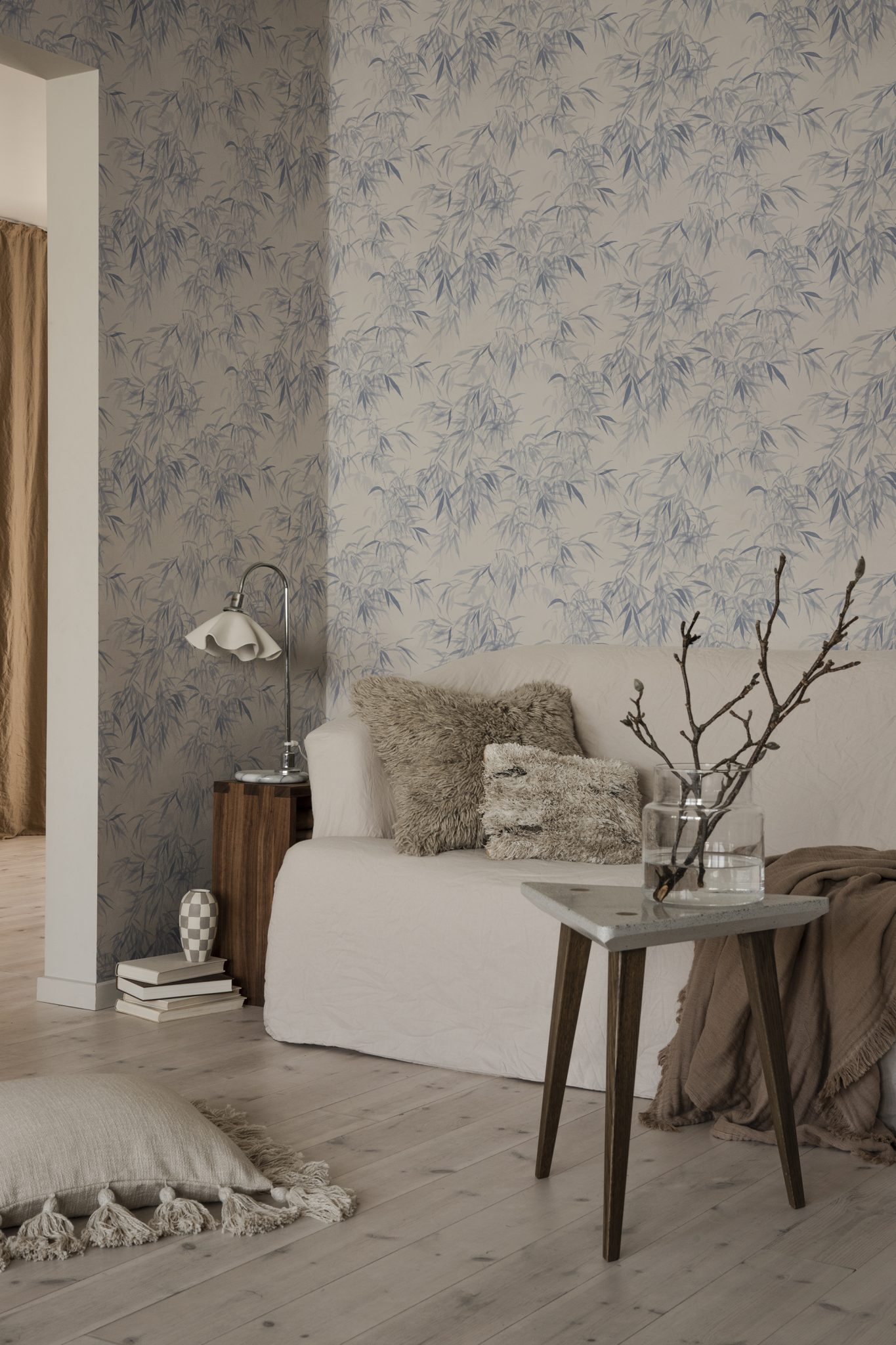 A bedroom with bamboo wallpaper, a white bed, and a small side table with a vase of branches.