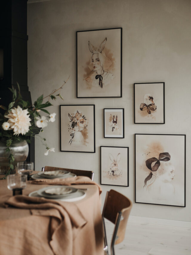 Framed watercolor art of rabbits and a woman with bunny ears, displayed on a wall above a table setting.