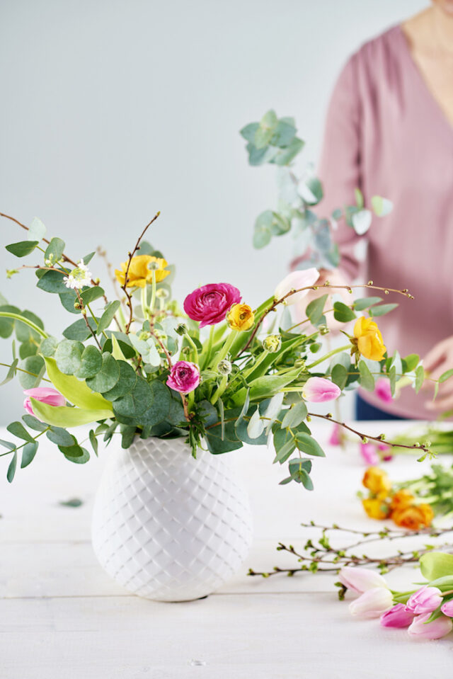 A vibrant bouquet of pink, yellow, and white flowers in a textured white vase.